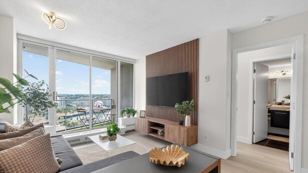 Ein modernes Wohnzimmer mit großem Fernseher, einer Couch, einem Couchtisch und einem Balkon mit Stadtblick.