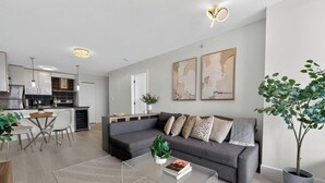 Ein modernes Wohnzimmer mit grauem Sofa, Couchtisch und einem Essbereich mit weißem Tisch und Stühlen.