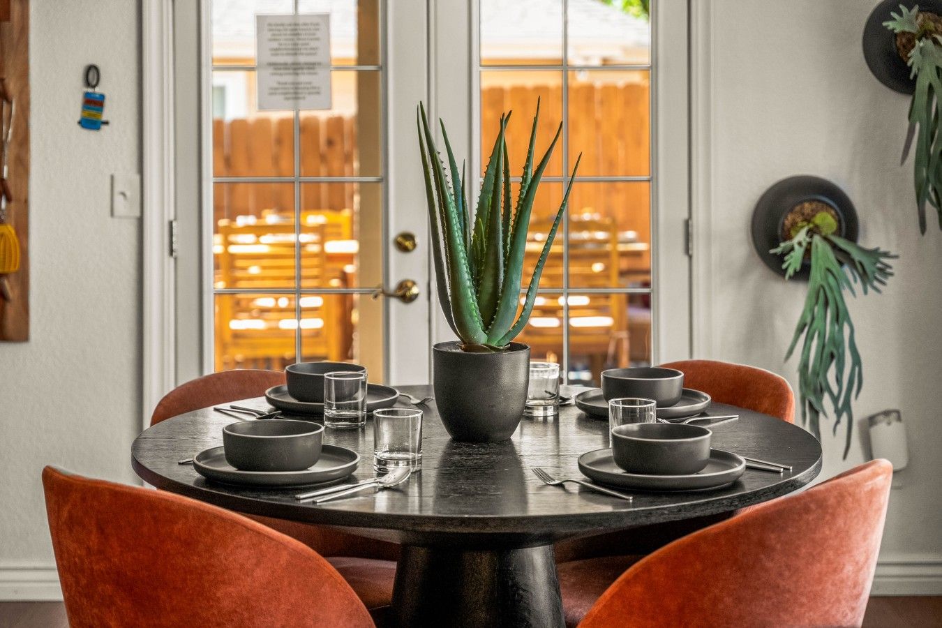 Una mesa de comedor dispuesta con platos, tazones y vasos, centrada alrededor de una planta en maceta.
