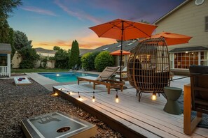 A poolside area with a wooden deck, lounge chairs, a decorative birdcage, and string lights. - Wanderlust Refuge - Quiet Home w/ Pool, Theater, Game Room, 5 min to airport (Grand Junction)