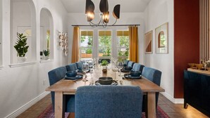 Un comedor con una mesa larga, sillas tapizadas en azul, un candelabro y ventanas grandes con cortinas.