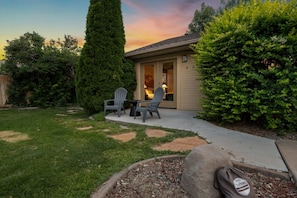 A residential property with a patio, two Adirondack chairs, a tall coniferous tree, and a well-maintained lawn. - Wanderlust Refuge - Quiet Home w/ Pool, Theater, Game Room, 5 min to airport (Grand Junction)