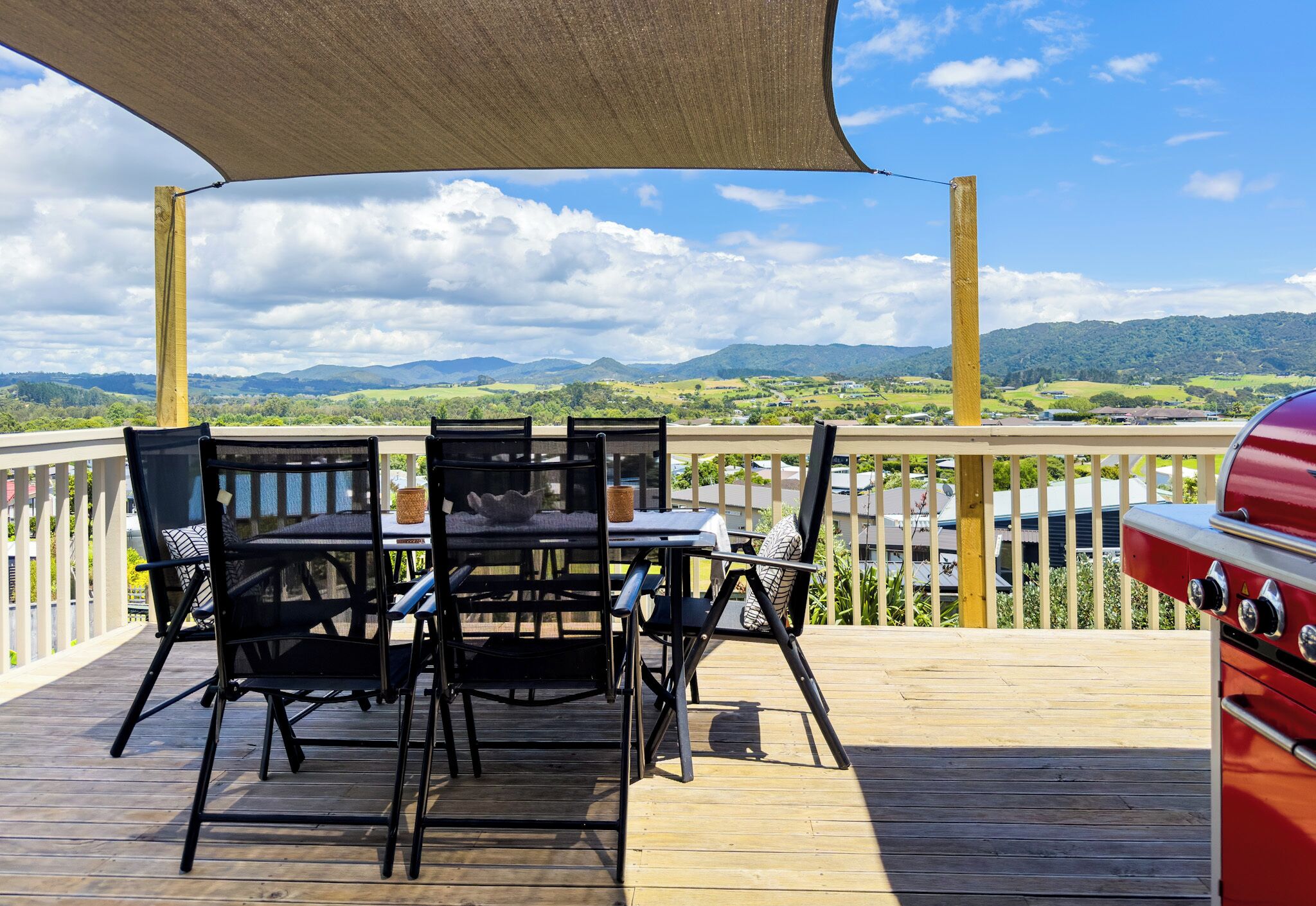 Un patio con tavolo e sedie, un barbecue e una vista panoramica su montagne e campi.