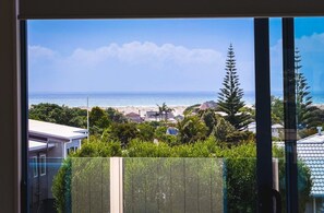 Blick durch ein Fenster auf eine Küstenlandschaft mit Strand, Meer und Wohnhäusern.