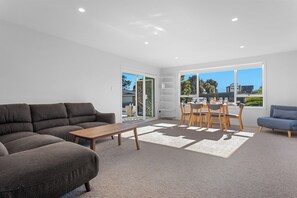 A modern living room with a sofa, coffee table, and dining area with chairs and a table. - Ocean Breeze Escape - Ohope Holiday Home (Ohope)