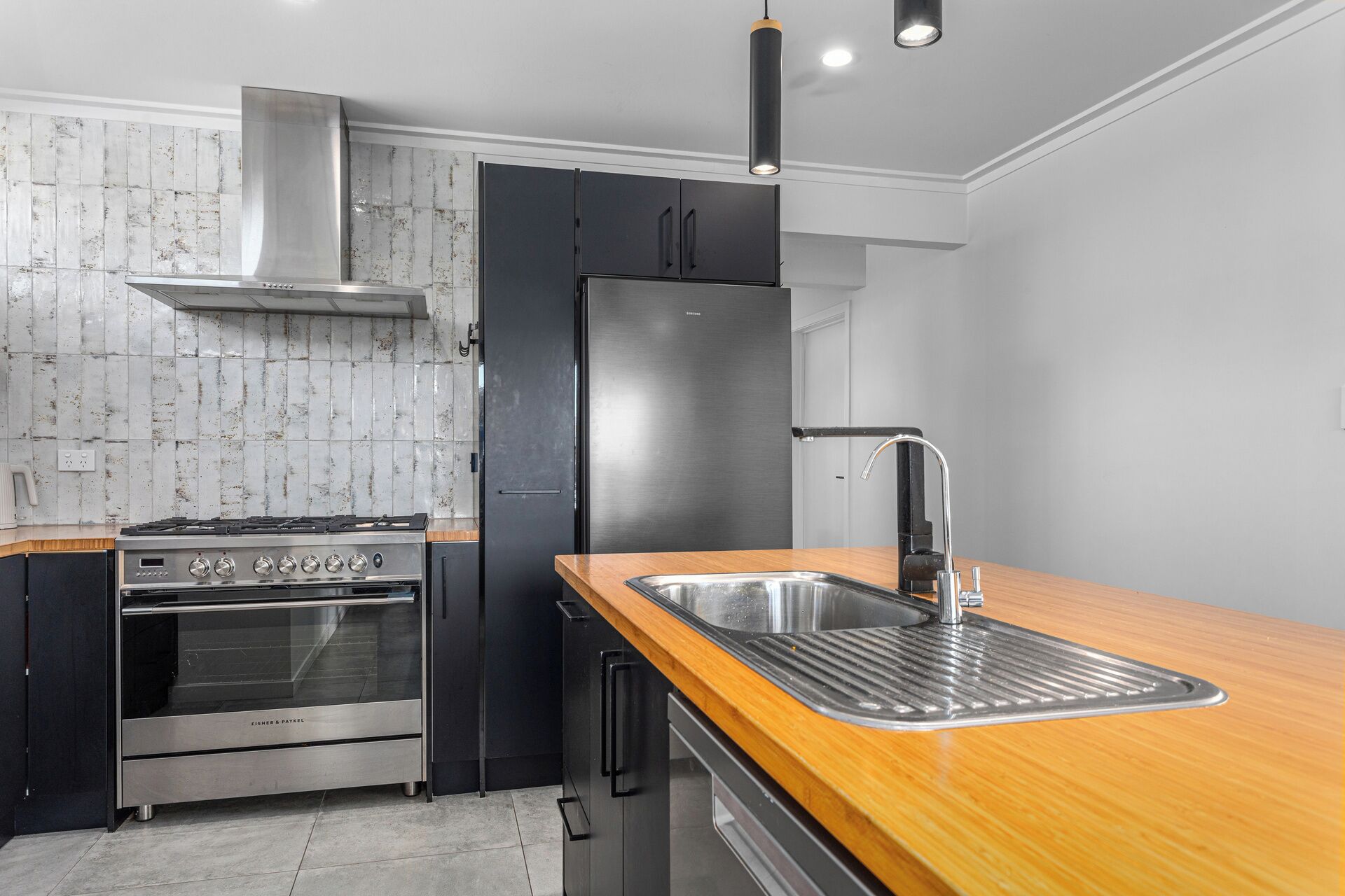 Una cocina con un refrigerador de acero inoxidable, un horno empotrado, un lavamanos con un grifo moderno y una encimera de madera.