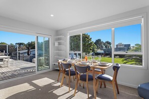 A modern dining room with a view of the backyard, a built-in grill, and a large window. - Ocean Breeze Escape - Ohope Holiday Home (Ohope)