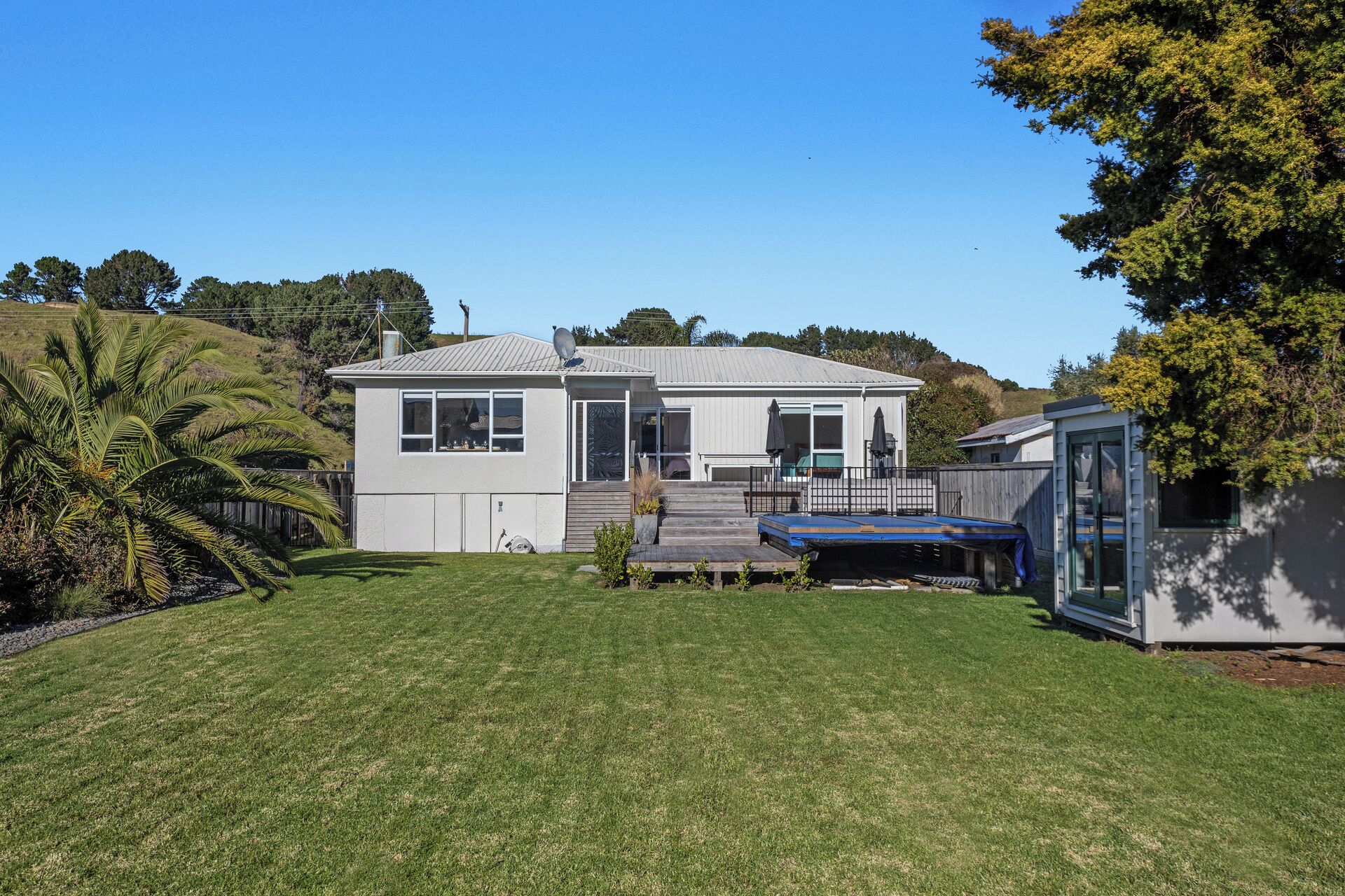 A single-story house with a front porch, a small deck, and a trampoline in the backyard.