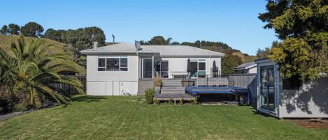 A single-story house with a front porch, a small deck, and a trampoline in the backyard.