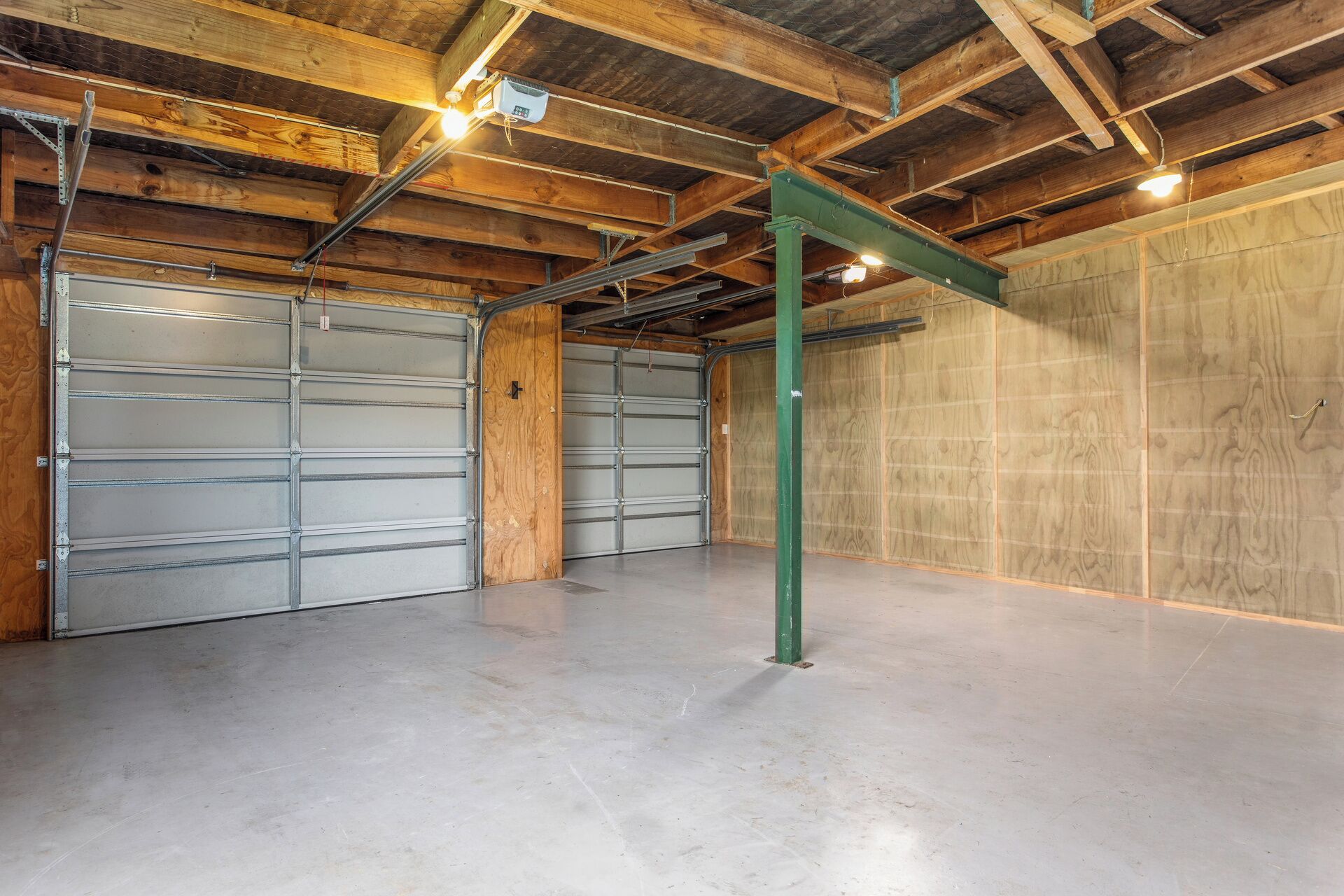 A spacious garage with two metal garage doors, a concrete floor, and wooden beams on the ceiling.