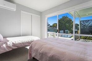A bedroom with two beds, a large window, and a view of the outdoors. - Ocean Breeze Escape - Ohope Holiday Home (Ohope)