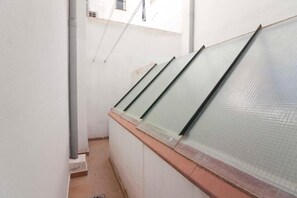 Ein schmaler Korridor mit gefliestem Boden, weißen Wänden und einem Fenster mit Metallrahmen.