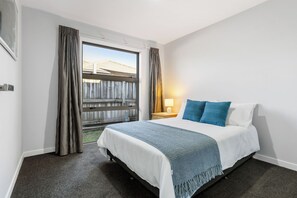 Ein Hotelzimmer mit Bett, Vorhängen, einem Fenster, einem Nachttisch und einer Lampe.