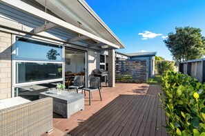 Eine moderne Außenpatio mit Korbmöbeln, einem Grill und Blick auf das Haus.