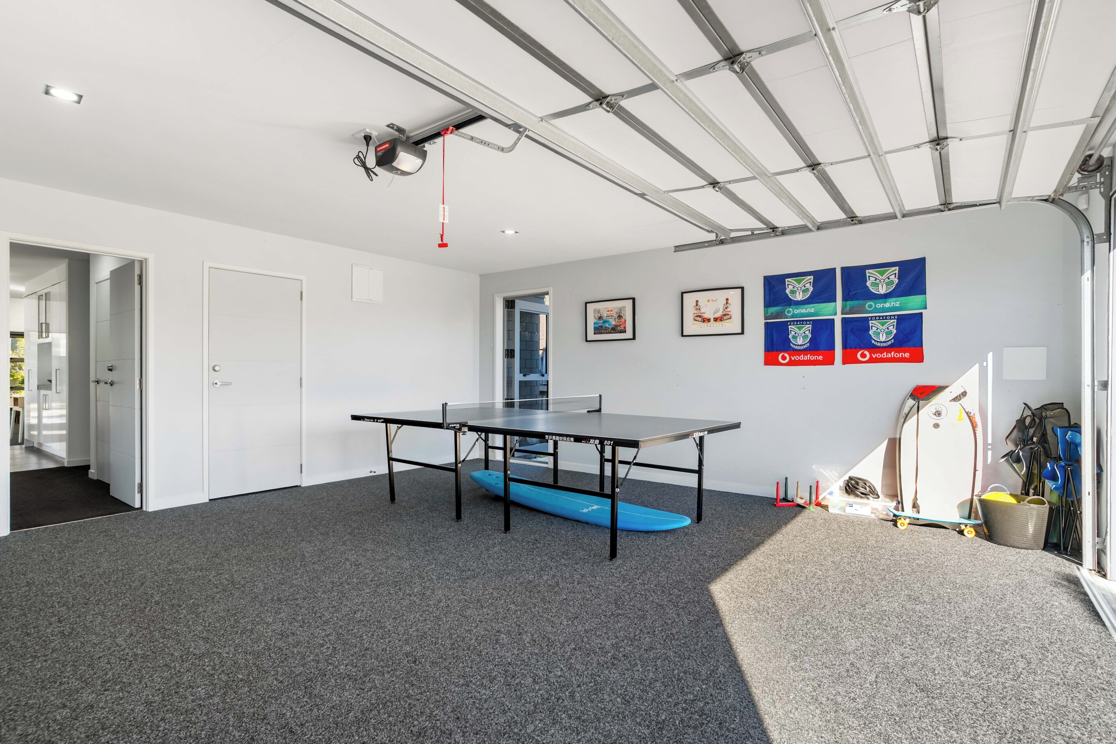 Een kamer met een tafeltennistafel, een blauw surfboard en een plafond met zichtbare balken.