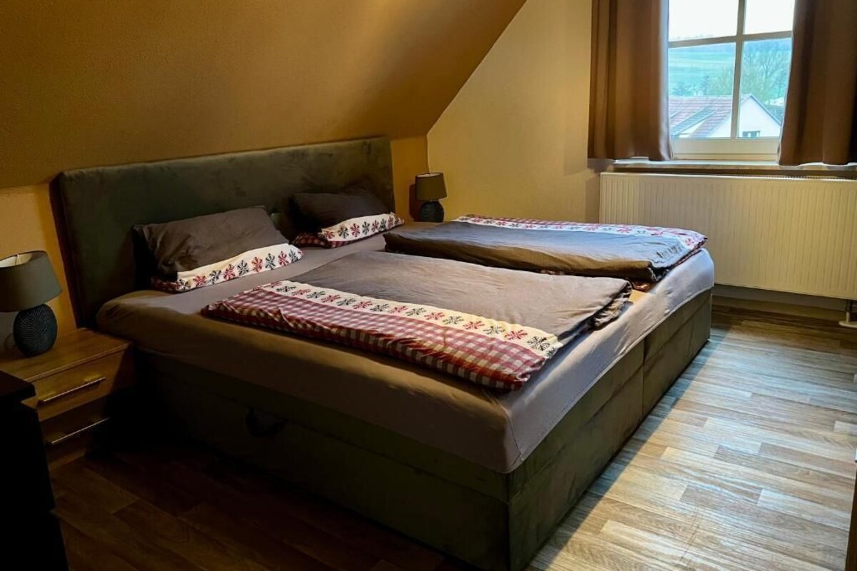 A bedroom with two beds, a nightstand, a lamp, and a window with curtains.
