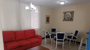 A living room with a red sofa, a wooden coffee table, and a dining area with white chairs and a round table. - Alquiler de Departamento, excelente ubicación. (Managua)