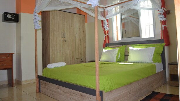 Een bed met houten frame en groene beddengoed, een houten kledingkast en een nachtkastje met een lamp.