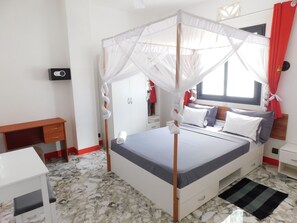 A bedroom with a bed, a desk, a wardrobe, and a window with curtains.