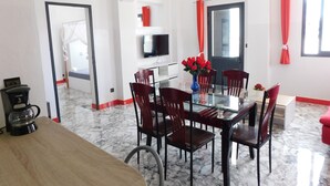 Een restaurantruimte in een hotel met een glazen tafel, rode stoelen, een aan de muur bevestigde televisie en een rood gordijn.