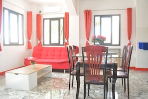 Une piÚce comprenant un canapé rouge, une table à manger, des chaises et une table basse.