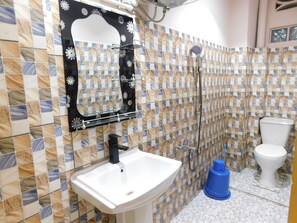Une salle de bain avec un mur carrelé, un lavabo, un miroir, une douche et des toilettes.