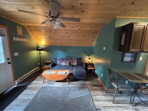 Ein gemütliches Zimmer mit Deckenventilator, einer Couch, einem kleinen Tisch, einem Stuhl und einem Schrank.