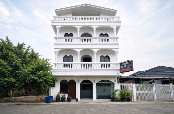 A multi-story white building with balconies, a sign for Hotel Wisma Yuli, and a clinic named Cintia Aesthetic Clinic.