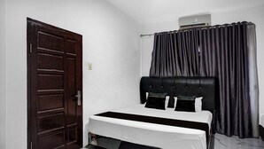 A bedroom with a single bed, a dark wooden door, and a window with black curtains. - Hotel O near Masjid Raya Al-Mashun forme (Medan)
