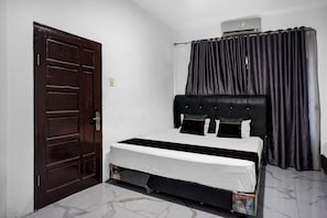 Un dormitorio con una cama individual, una puerta de madera oscura y una ventana con cortinas negras.