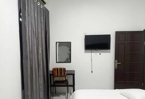 A bedroom with a bed, a TV mounted on the wall, a chair, a door, and a curtain.