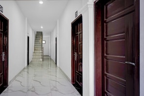 Un pasillo con piso de mármol, puertas de madera y una escalera que conduce a un nivel superior.