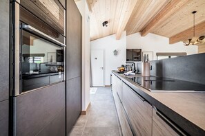 Eine moderne Küche mit dunklen Schränken, einer Holzbalkendecke und einer großen Kochinsel mit schwarzer Arbeitsplatte.