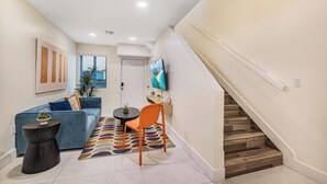 A modern living room with a sofa, a coffee table, a chair, a rug, and a staircase. - 3BR Ft Lauderdale Townhome + Game Room + Parking (Fort Lauderdale)