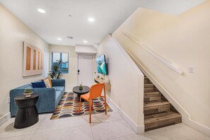 Uma sala de estar moderna com um sofá, uma mesa de centro, uma poltrona, uma televisão e uma escada.