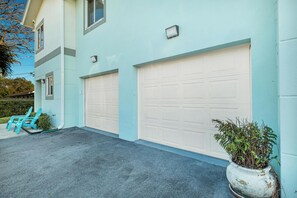A two-story building with two garage doors, a potted plant, and a small garden area with chairs.