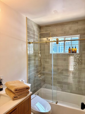 Ein Badezimmer mit einer Dusche in Glasabtrennung, einer Badewanne, einer Toilette und einem Waschtisch mit einem Handtuch.