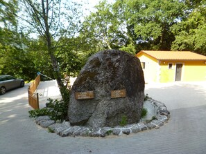 A large rock with two directional signs, a paved area, and a yellow building in the background. - Little house in Geres (Vieira do minho)