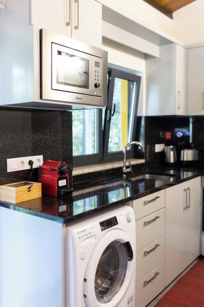 A compact kitchen with a microwave, coffee maker, and a washing machine. - Little house in Geres (Vieira do minho)
