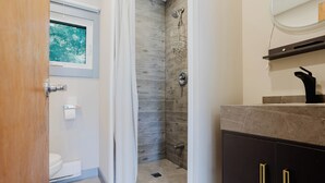 A bathroom with a shower, toilet, and vanity with a mirror. - 2-Bedroom Cottage #4 (Nobel)