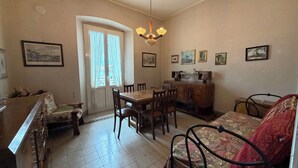 Et spiseområde med et bord, stole, en sofa, et træskab og en dør med gardiner.