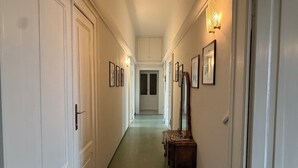 En gang med hvide døre, indrammede billeder og et spejl på højre væg.