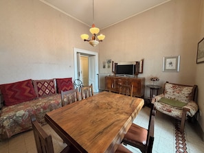 Ein Essbereich mit Holztisch, Stühlen, einer Couch und einem Fernseher auf einem Schrank.