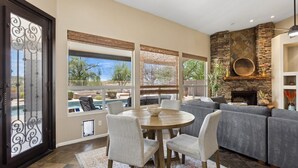 A living room with a stone fireplace, a pool view, and a dining area with chairs.