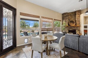 A living room with a stone fireplace, a pool view, and a dining area with chairs. - Ahwatukee Foothills Home | Heated Pool | Grill (Phoenix)