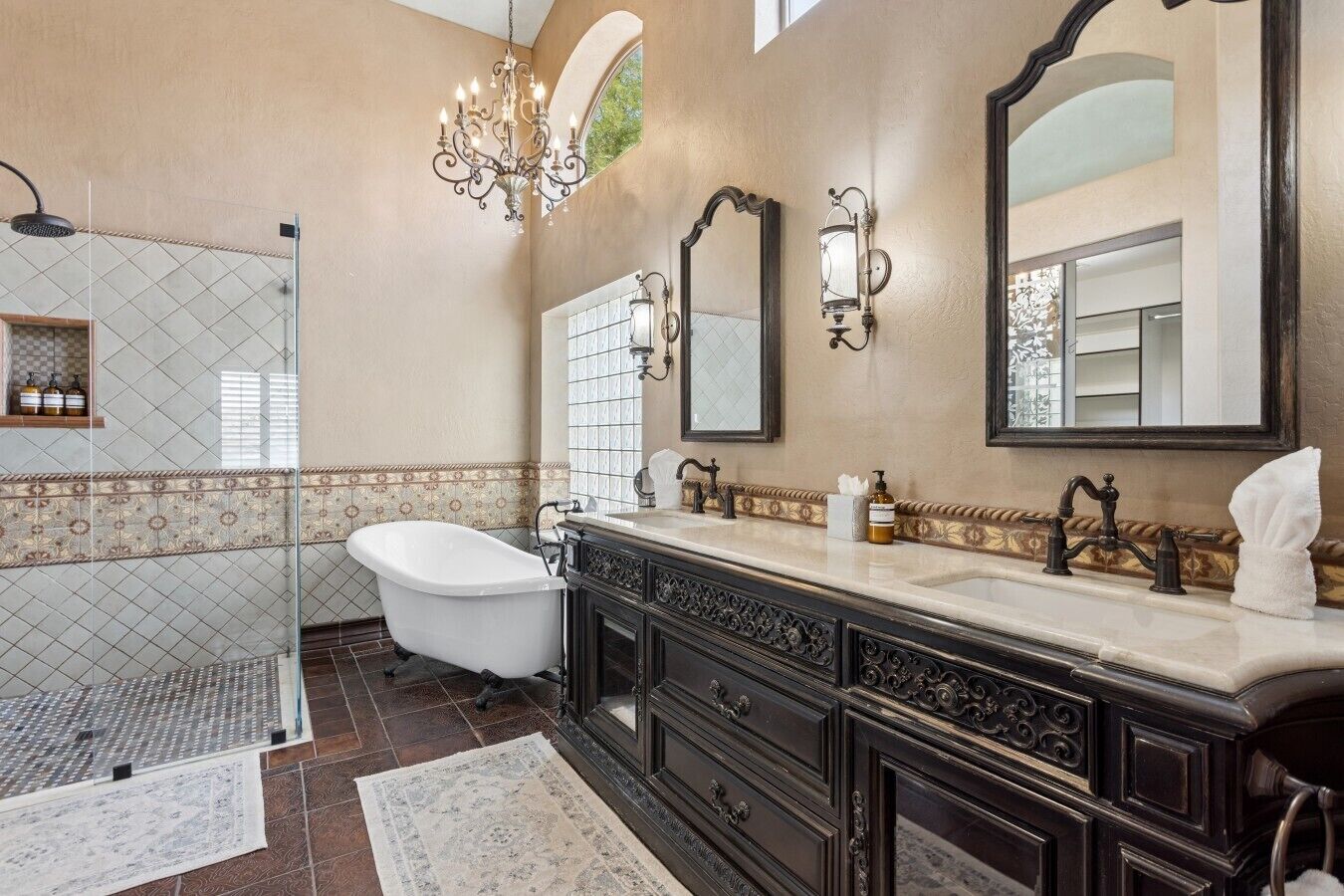 A bathroom with a freestanding bathtub, a large mirror, a chandelier, and a tiled shower area.