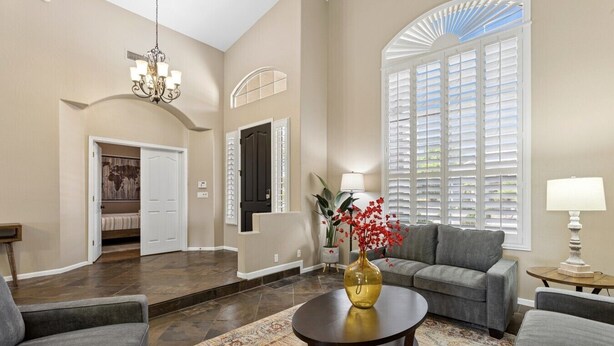 A spacious living room with a large window, a chandelier, and a sofa.