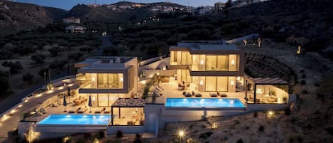 Una casa moderna de dos pisos con piscina, mobiliario exterior y vistas a un paisaje montañoso.