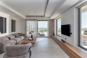 Un soggiorno moderno con un divano componibile, un tavolino, un televisore a schermo piatto e un'ampia finestra con vista sul mare.