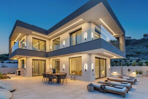 Ein modernes, zweistöckiges Haus mit Balkon, großen Fenstern und einer Außenbereich-Sitzgelegenheit.